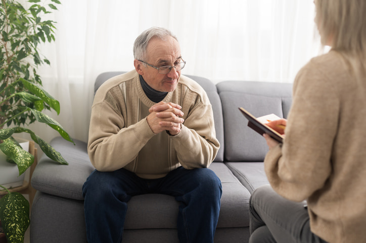 Senior man sitting on a couch across from a female therapist talking